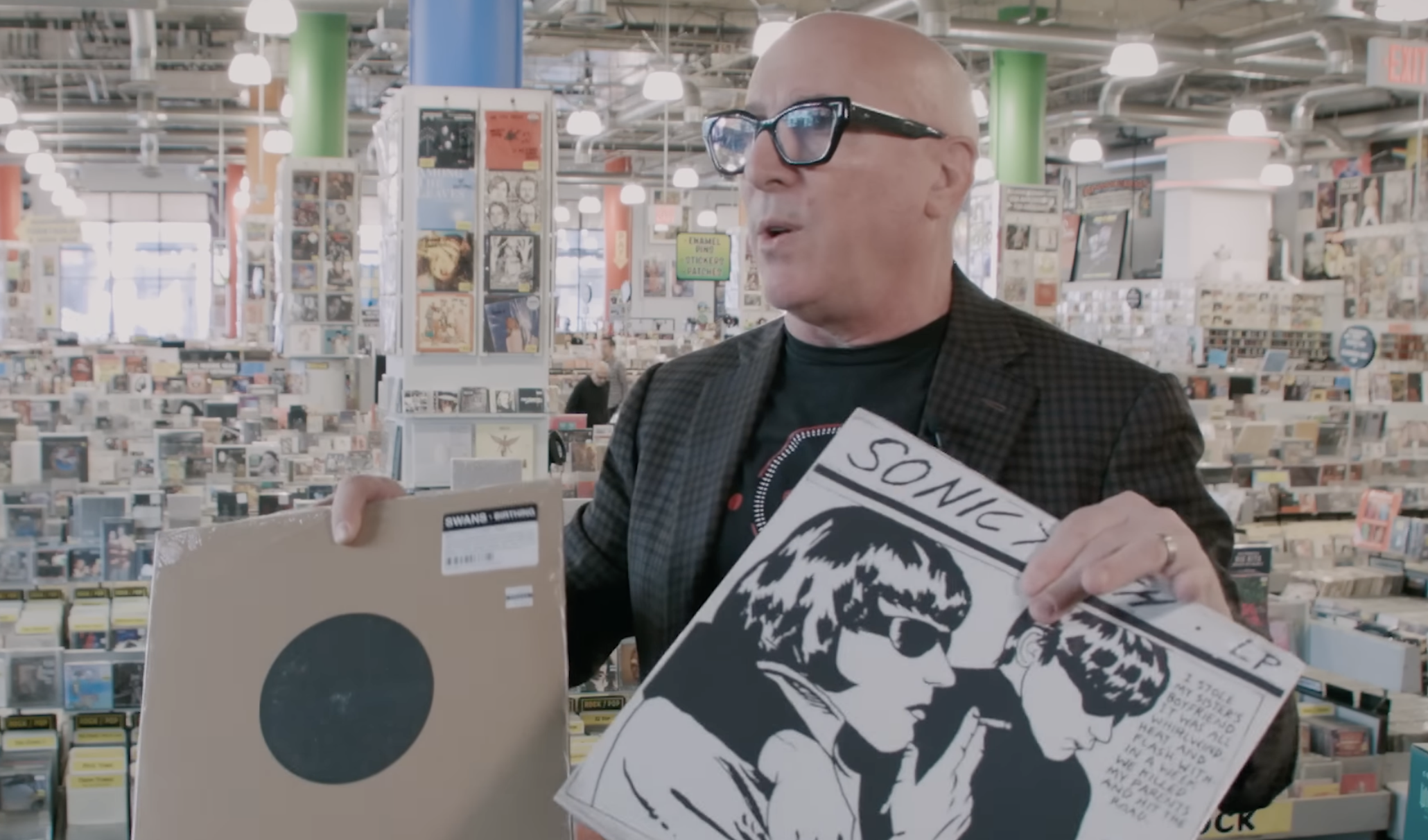 Maynard James Keenan holding vinyl records by Swans and Sonic Youth while posing for a photo.