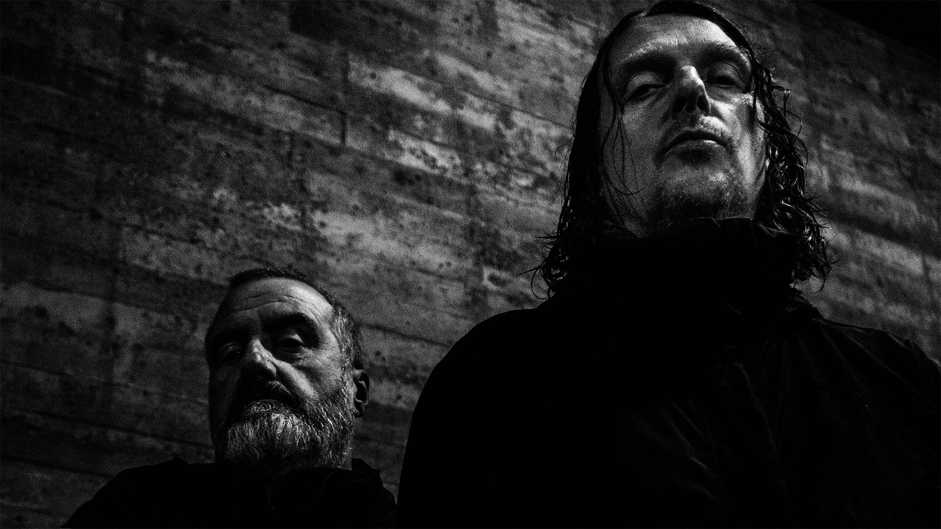 Studio promotional photo of Godflesh featuring members Justin Broadrick and G. C. Green posed against a dark industrial backdrop.