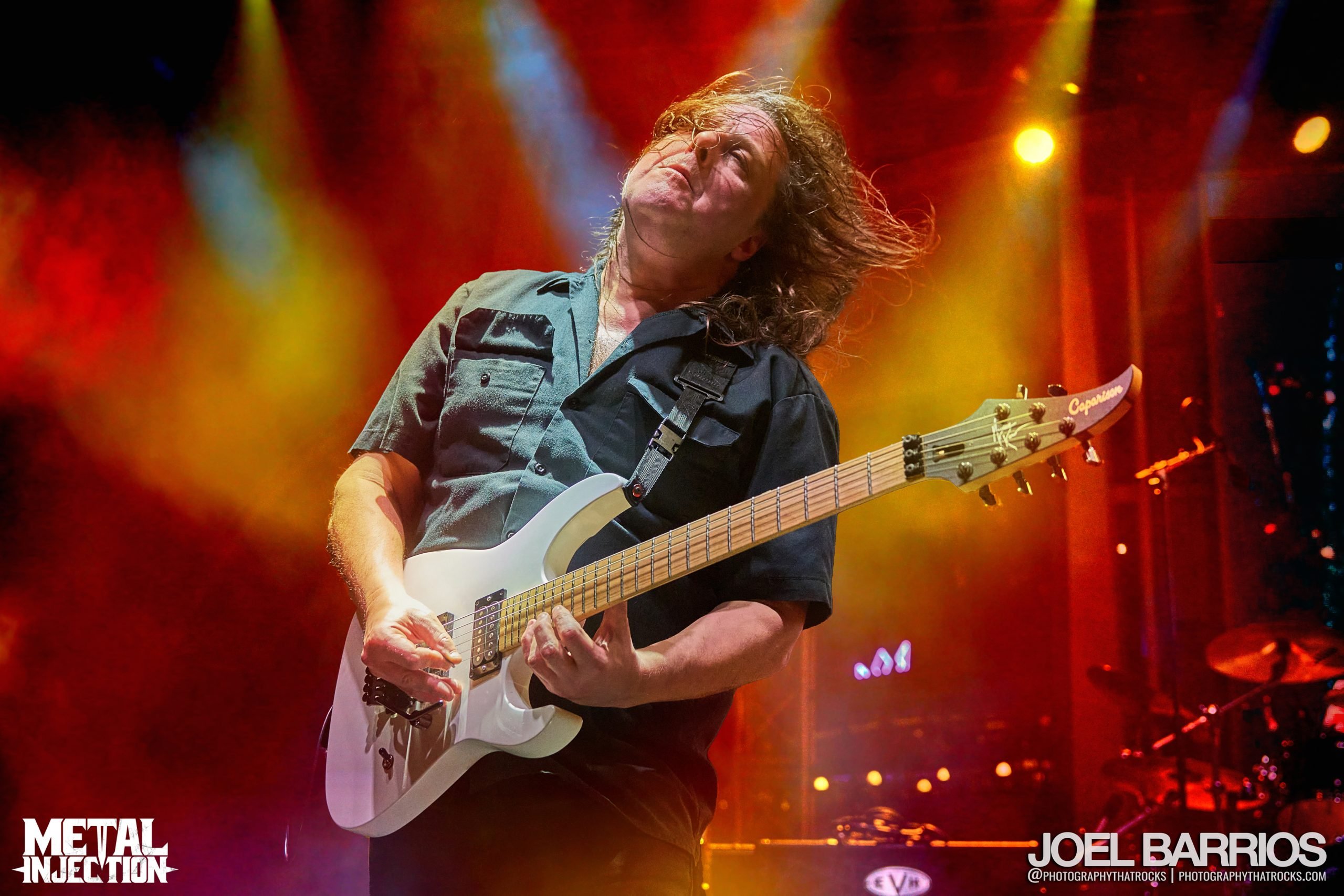 Michael Romeo playing guitar on stage during a live Symphony X concert with dramatic stage lighting.